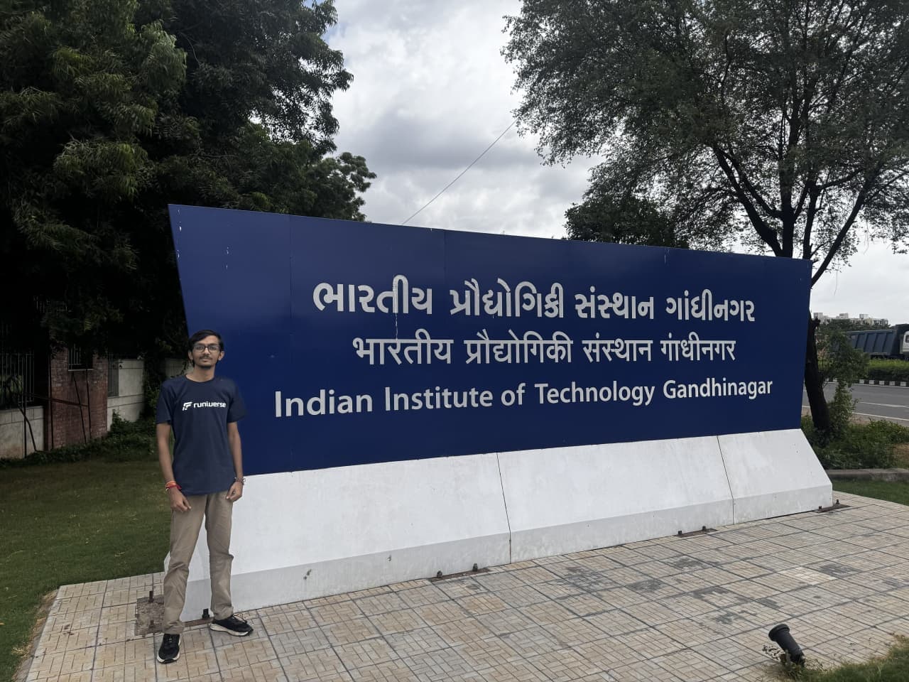 A Runiverse team member standing beside the Indian Institute of Technology Gandhinagar entrance sign.